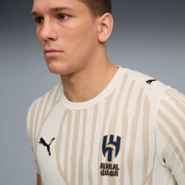 A model wears a striped white and beige t-shirt with logos against a grey backdrop.