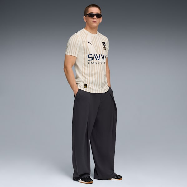 A model poses against a grey backdrop, wearing a striped t-shirt, wide trousers and sunglasses.