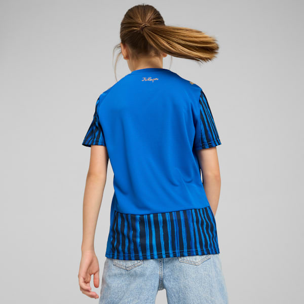 A model with a ponytail, against grey, wears a blue t-shirt and light blue denim shorts.