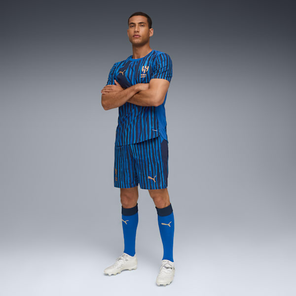 A model with crossed arms wears a blue striped kit against a grey backdrop.
