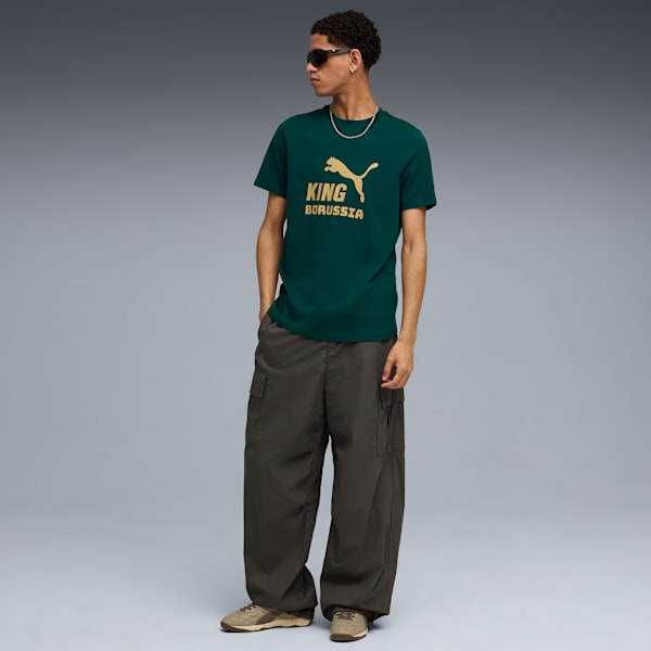A model stands against a grey backdrop wearing a green t-shirt, cargo trousers, and trainers.