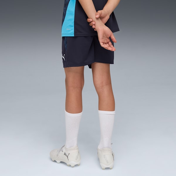 A model in front of grey background wearing navy shorts, top, white socks and shoes.