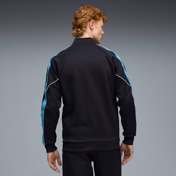 A model stands against a grey backdrop, wearing a black jacket with blue details.