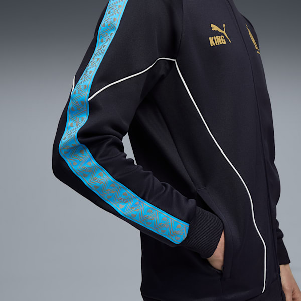 Against grey, a person wears a black jacket with blue patterned stripes and the word 'KING'.