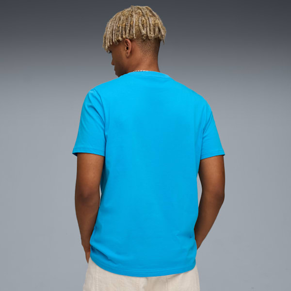 A model faces away from the viewer wearing a blue t-shirt against a grey backdrop.