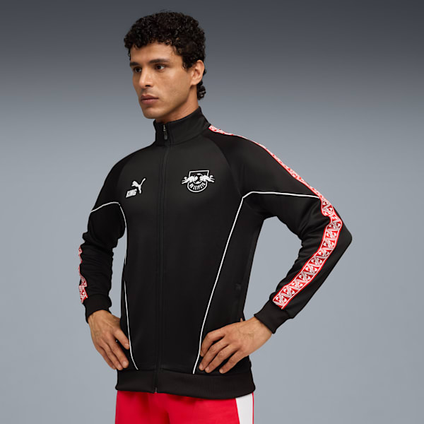 A model poses against grey wearing a black jacket with red details and red trousers.