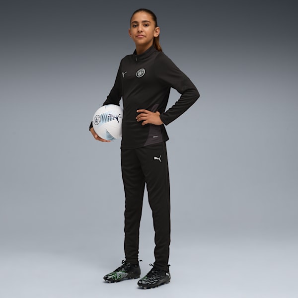 A model poses with a football against a grey backdrop, wearing a black training kit.