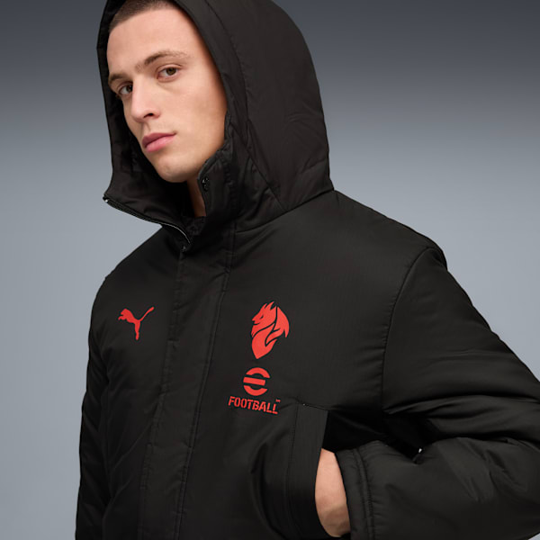 Against a grey backdrop, a model poses in a black hooded jacket with red logos.