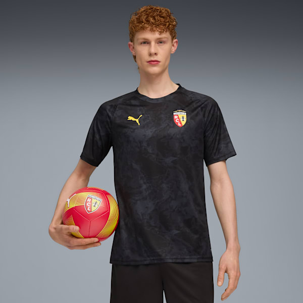 A model holds a red and yellow football in front of a grey backdrop, wearing a black t-shirt.