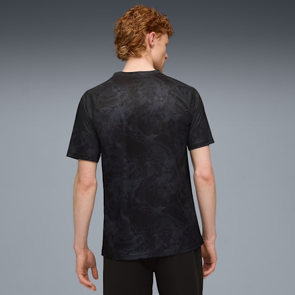 A model faces away from the camera in front of a grey background wearing a patterned black t-shirt.