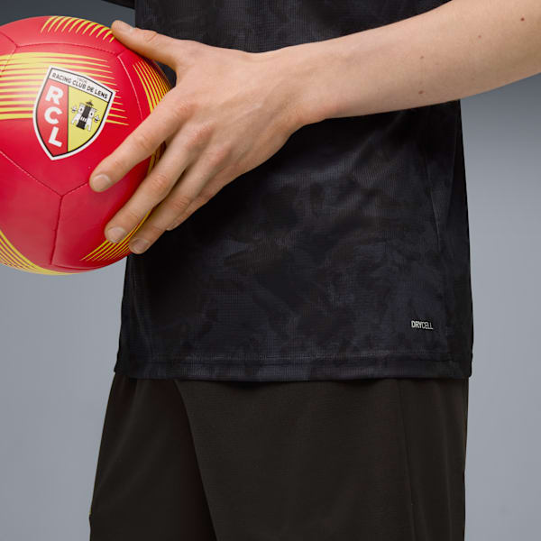 A person holds a red football with the Racing Club de Lens logo, wearing a black shirt.