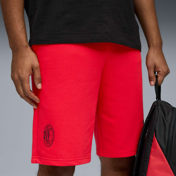 A model wears red shorts with a logo and a black t-shirt against a grey background.