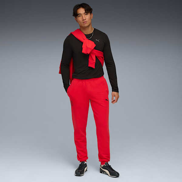 A model stands against a grey backdrop, wearing a black top, red trousers and trainers.
