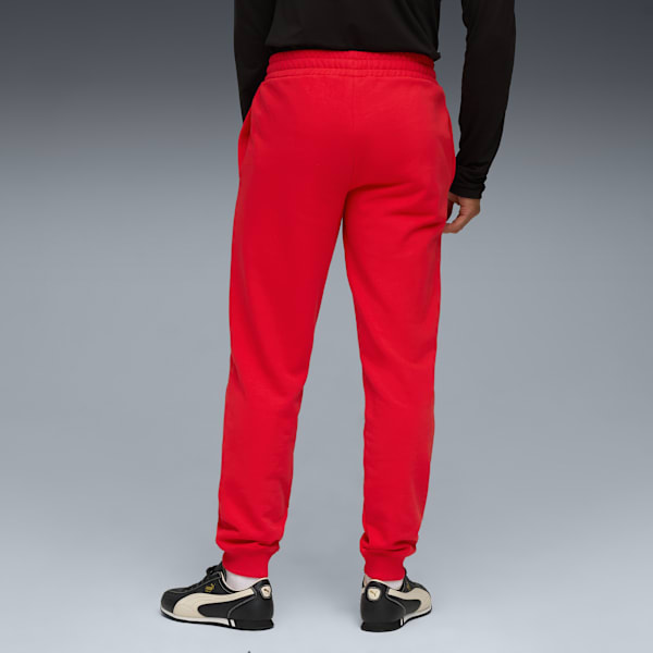 Seen from behind, a model wears red jogging bottoms and trainers against a grey backdrop.