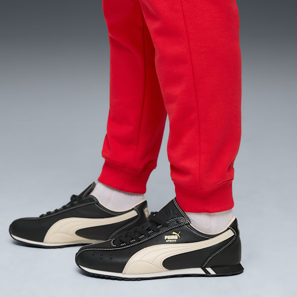 Against grey, a person wears red joggers and black/cream running shoes.