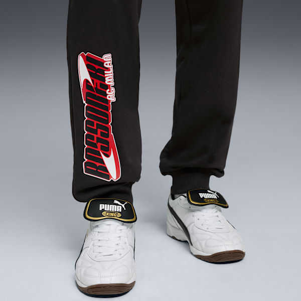 On grey, a person wears black AC Milan joggers and white Puma King trainers.