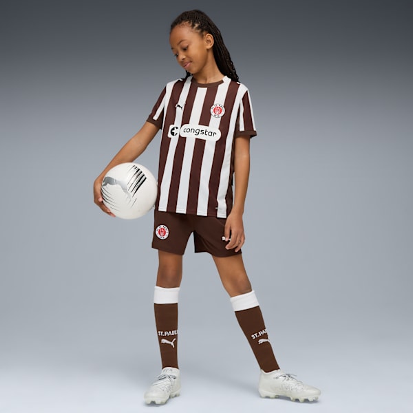 A model poses with a football against a grey backdrop, wearing a brown and white kit.