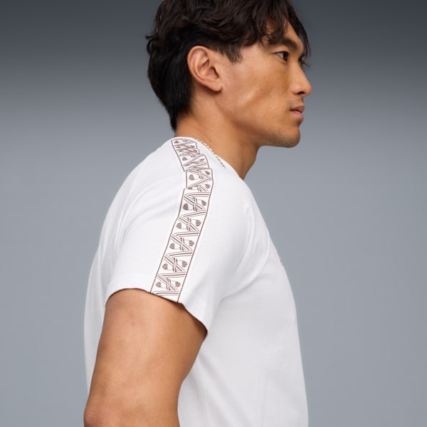 A model in profile against grey wears a white t-shirt with patterned shoulder detail.