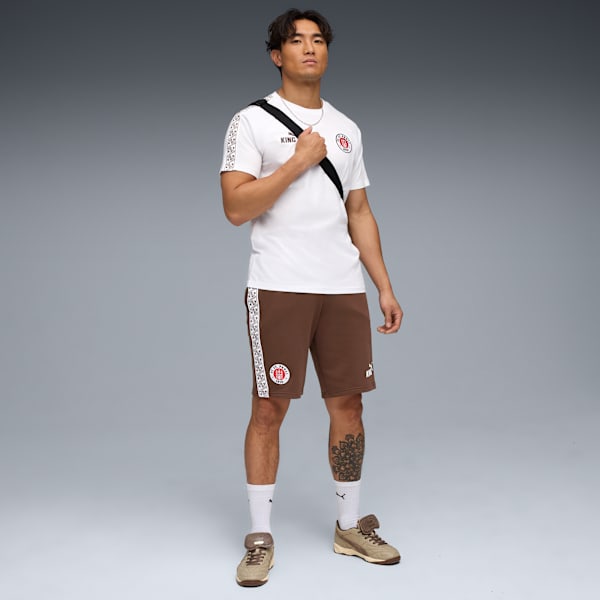On grey, a model poses wearing a white t-shirt, brown shorts and trainers.