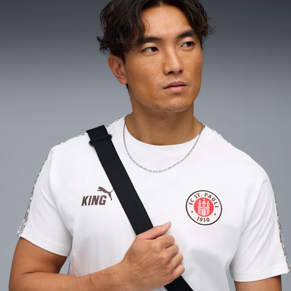 Against grey, a model wears a St. Pauli shirt with a black bag strap.