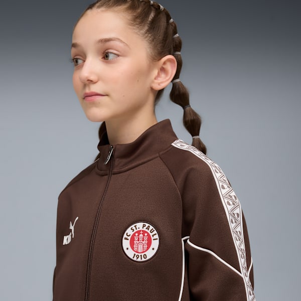 Against a grey backdrop, a model wears a brown jacket with the FC St. Pauli logo.