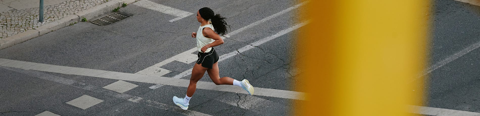 On a city street, a woman runs wearing a light top, dark shorts and light-coloured running shoes.