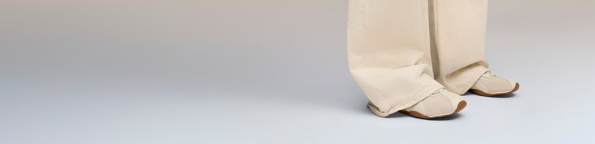 On a grey backdrop, a person wears beige trousers and matching trainers.