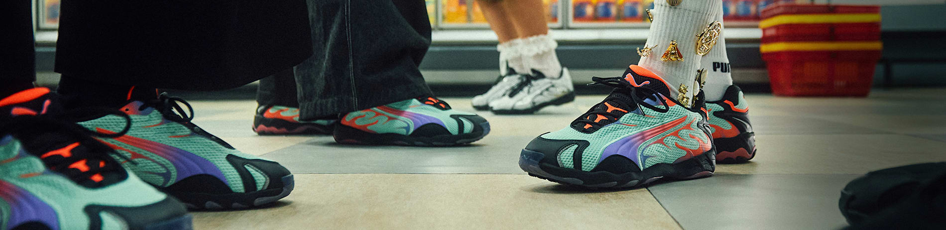 Close-up of people wearing teal and purple trainers with orange accents in a shop aisle.