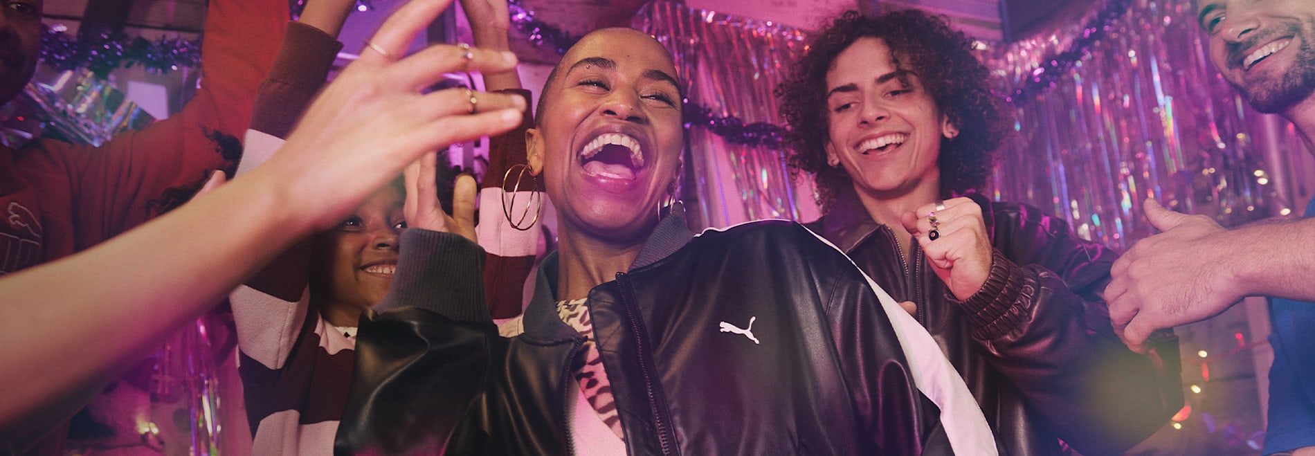A group of smiling people celebrate against a shiny, festive backdrop.