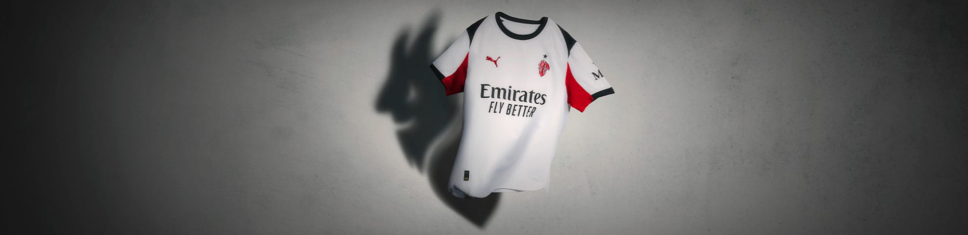 Against a grey backdrop, a white football jersey with red and black trim is displayed.