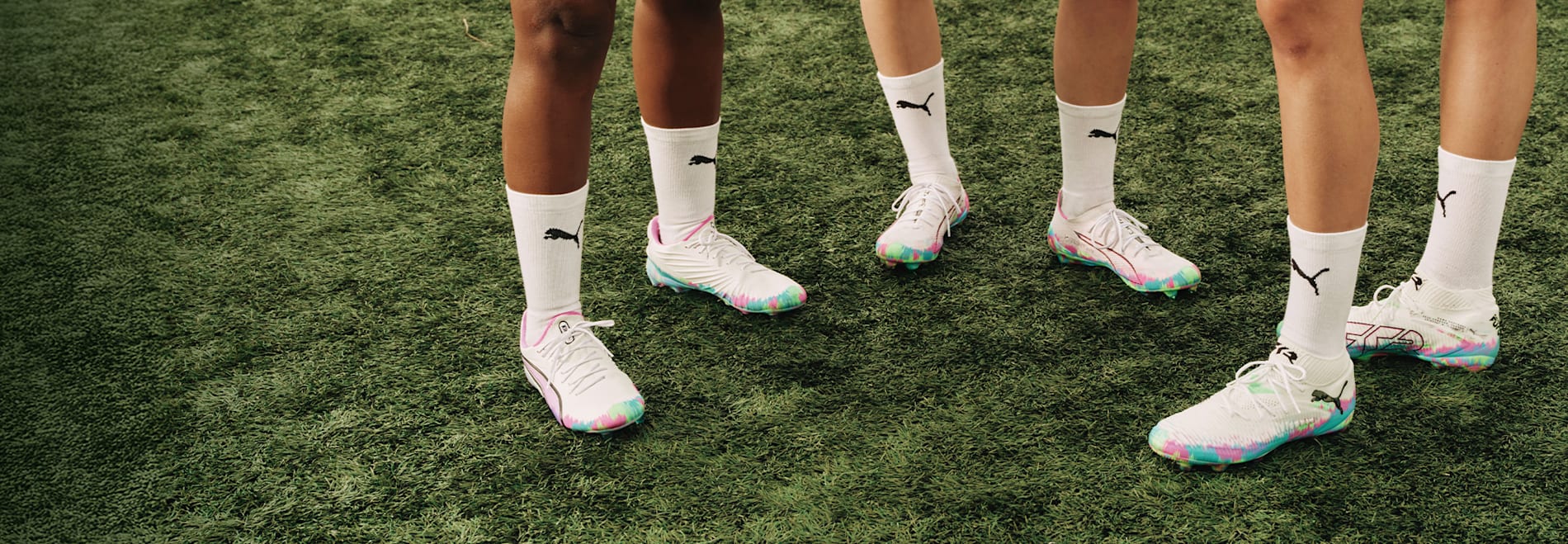 On grass, models wear white football boots with colourful soles and matching socks.