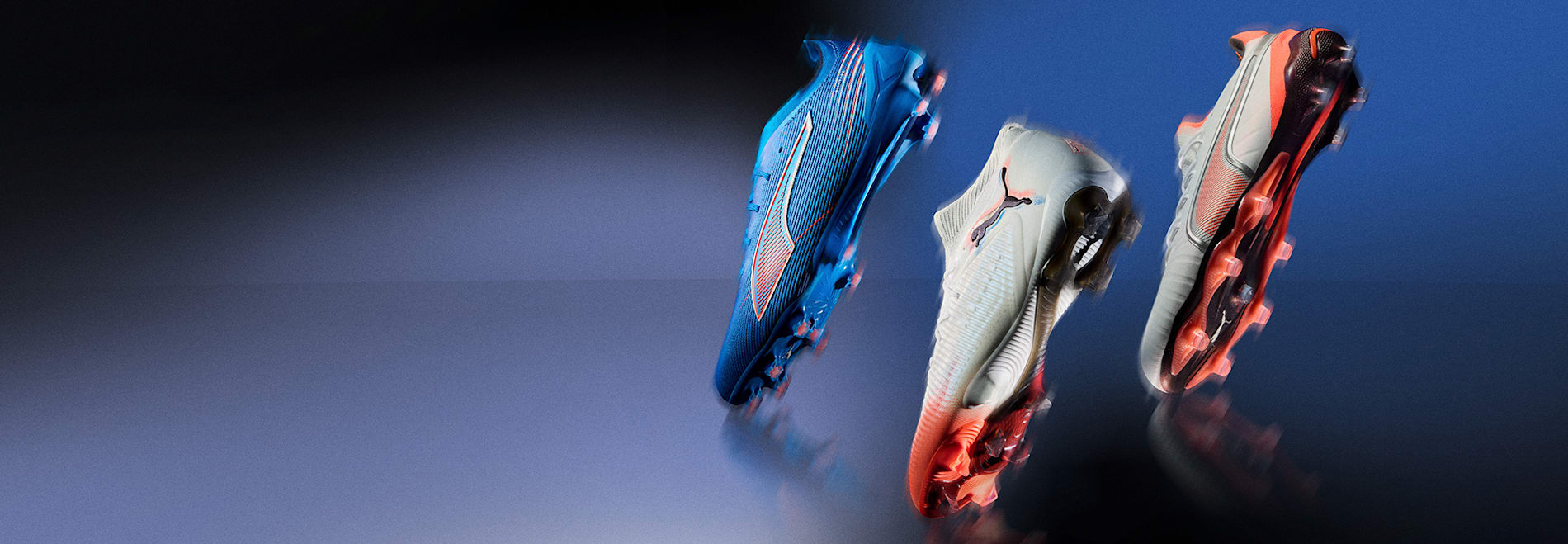 Three football boots, in blue, white and grey with orange details, are displayed on a blue backdrop.