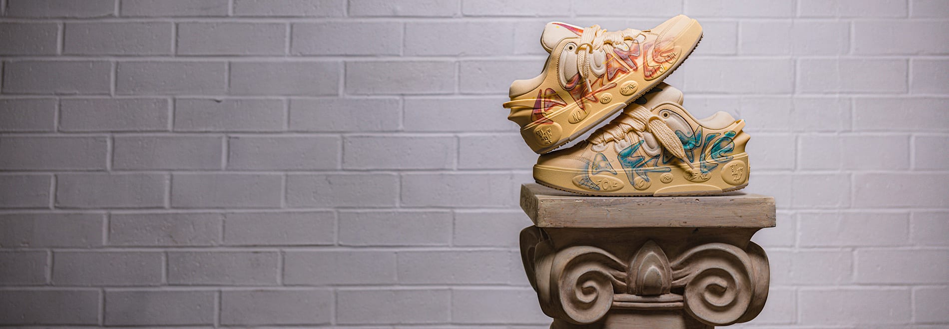 Stacked beige trainers with colourful airbrush design displayed on a decorative pillar.