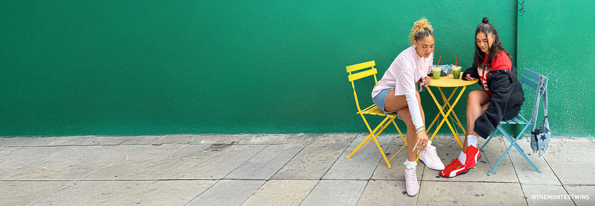 Deux mannequins en tenues sportives sont assises à une table de café devant un mur vert vif.