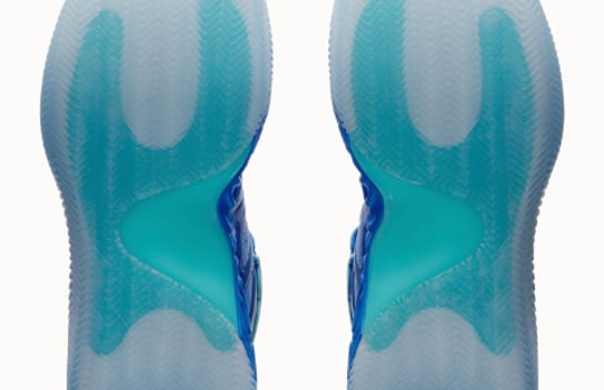 Close-up shows the soles of two blue and turquoise basketball shoes on white.