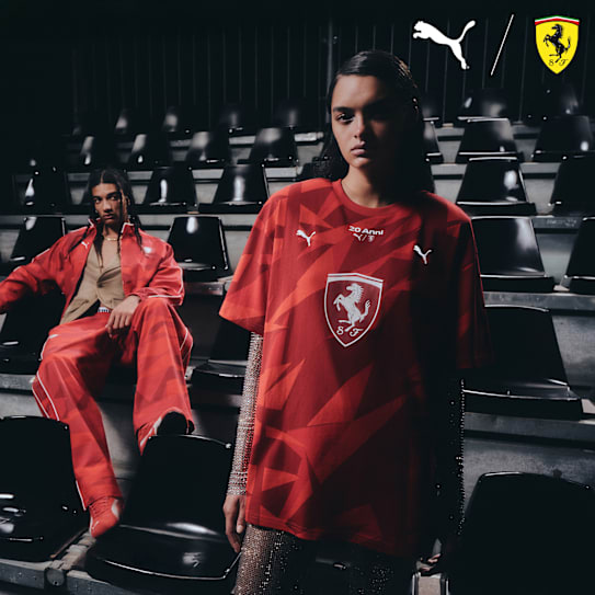 Two models pose in red Puma/Ferrari gear against a backdrop of stadium seating.