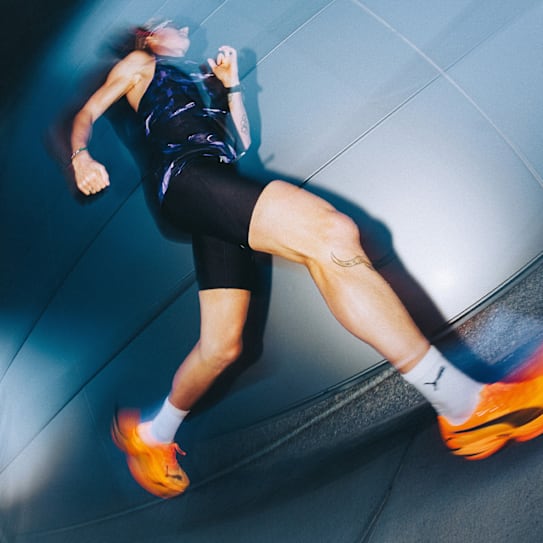 Drie hardlopers sprinten, aangemoedigd door een menigte, gekleed in sportkleding en schoenen.