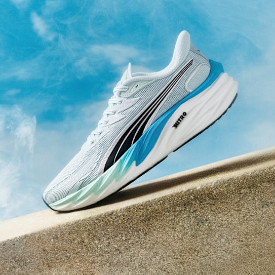 Ein hellblauer Laufschuh mit schwarzen Streifen steht auf einem Betonsims vor blauem Himmel.