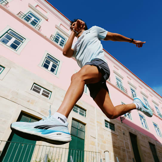 Un homme en tenue de sport saute en l'air et porte des chaussures de course Velocity Nitro bleu clair.