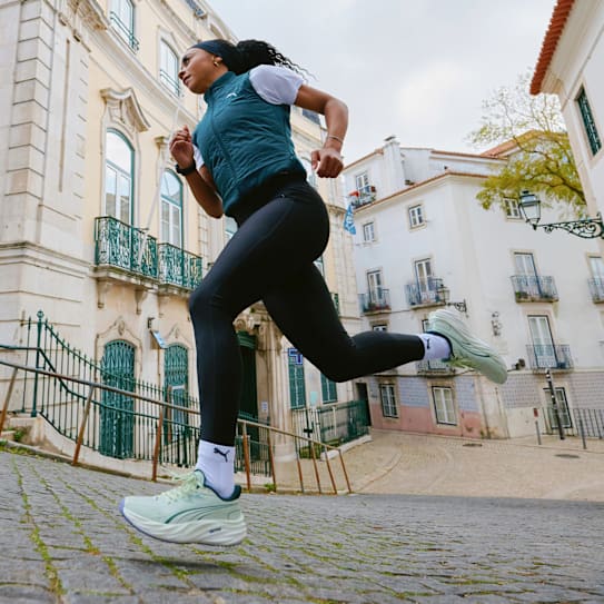 Een vrouw rent op een geplaveide straat, gekleed in hardloopkleding en lichtgroene sneakers.