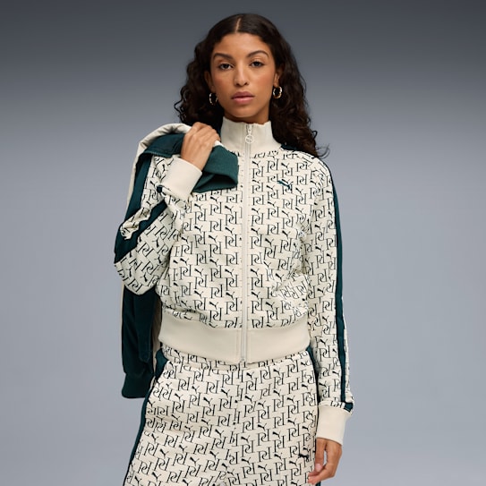 Against a grey backdrop, a model wears a monogrammed tracksuit and holds a jacket.