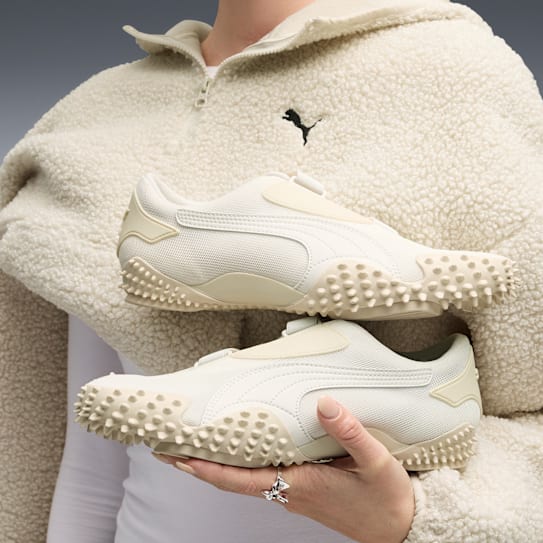 Person wears patterned gold trousers with white stripe and cream suede trainers.