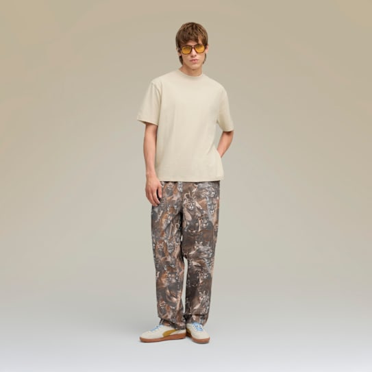 Sur un fond uni, un mannequin pose avec un t-shirt, un pantalon à motifs et des baskets.