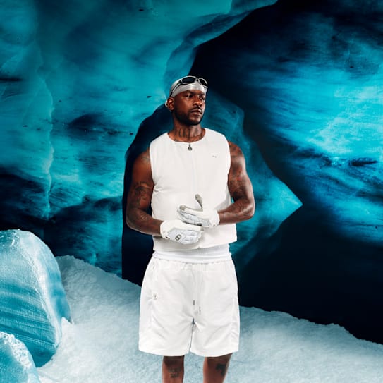 Un homme en tenue de sport blanche pose devant une grotte de glace bleue.
