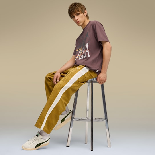 Un modèle assis sur un tabouret, portant un t-shirt, un pantalon doré à rayures et des baskets crème.