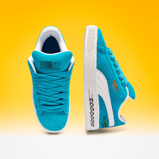 Tegen een gele achtergrond staan twee blauwe Suede XL Super Puma-trainers.
