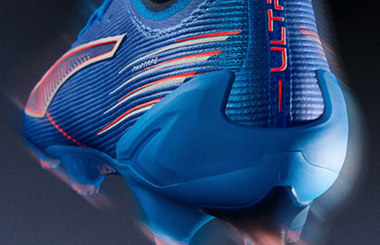 Close-up of a blue football boot with orange and white details against a dark background.