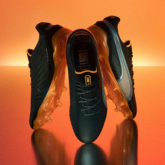 A grey and orange football boot is suspended against a blurred blue background.