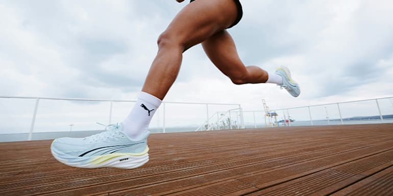 Eine Läuferin schreitet vorwärts, mit hellblauen Laufschuhen und weißen Socken auf Holz.
