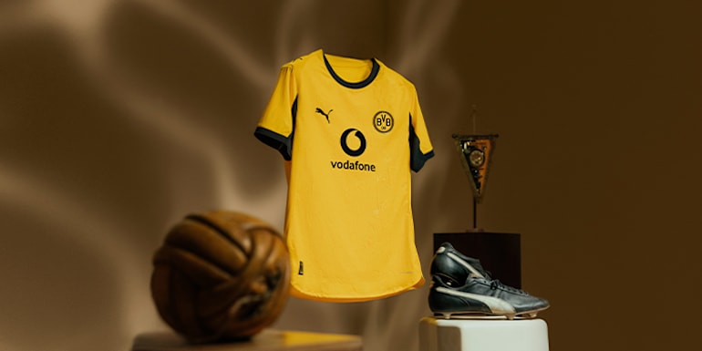 A yellow football shirt is displayed with a ball, boot and pennant against a brown backdrop.